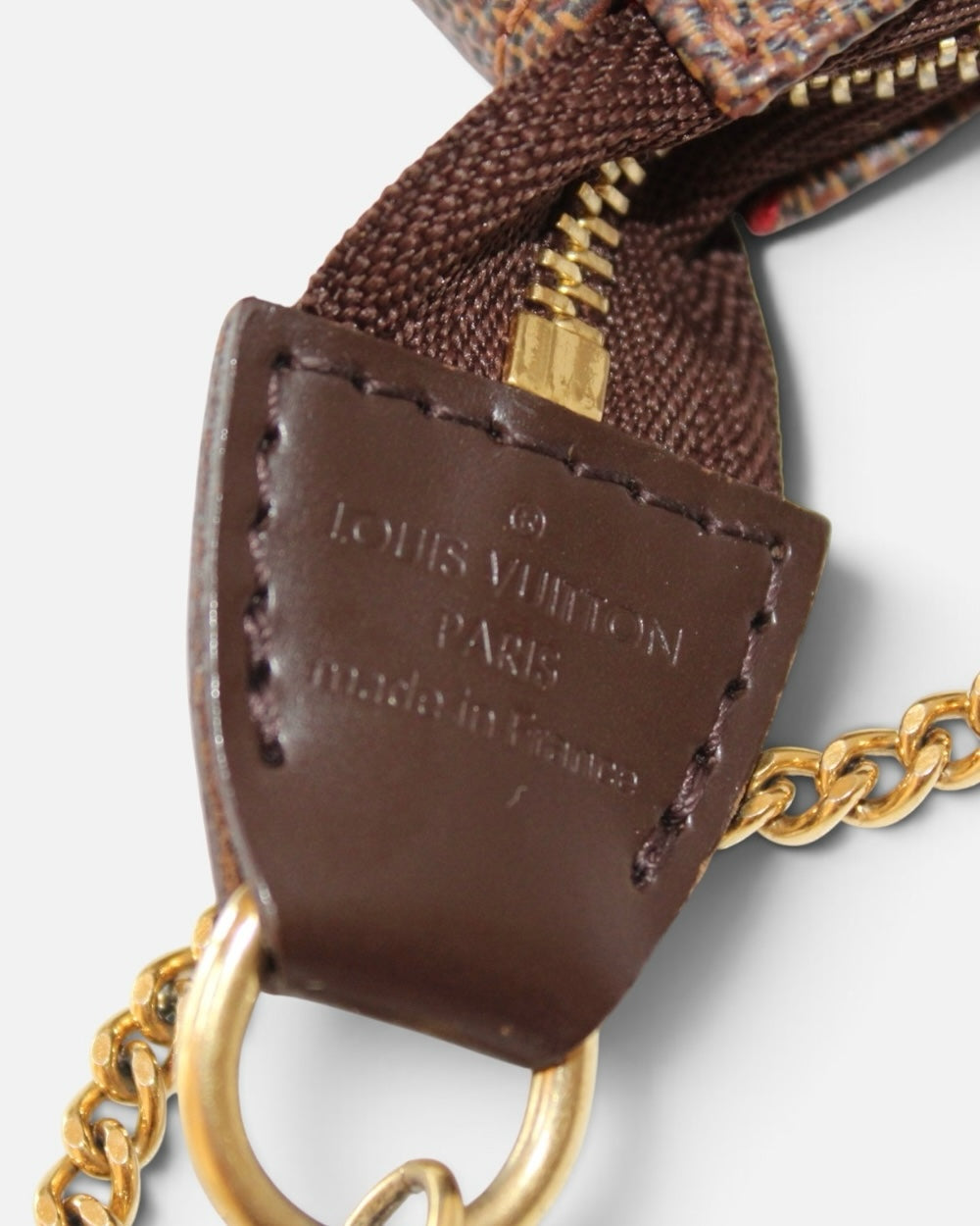 Detalle de etiqueta de cuero café con logo Louis Vuitton y cadena dorada en bolso Hibiscx's Archive Damier Ebene