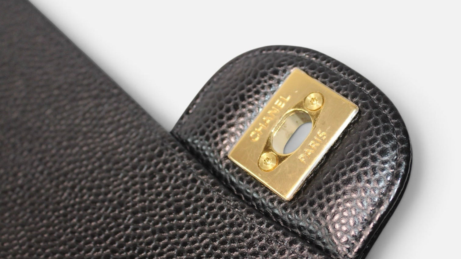 Detalle del cierre dorado con logo de Hibiscx's Archive en bolso CHANEL de piel de caviar negra acolchada
